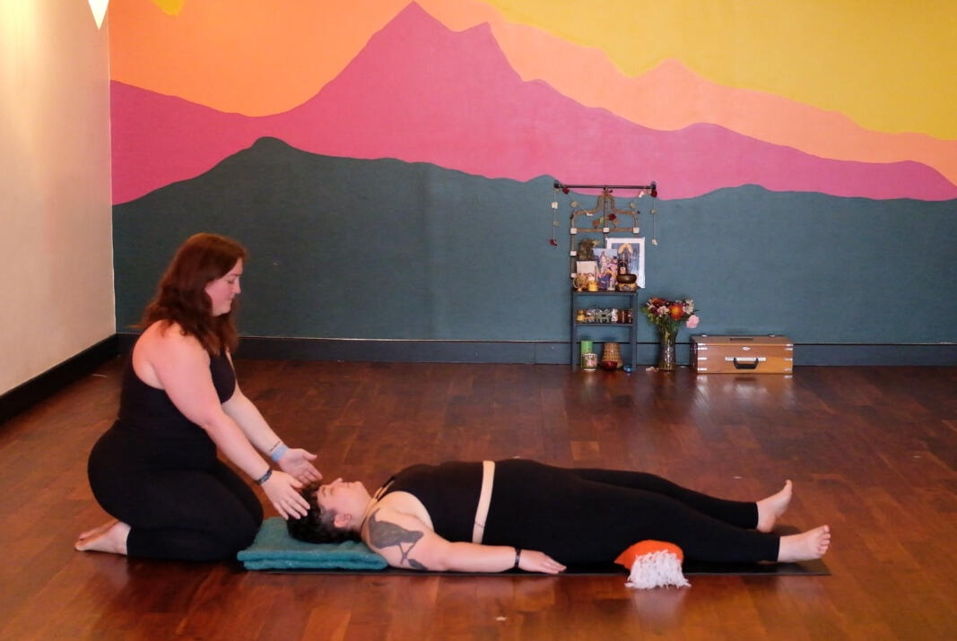 Steph sitting on her knees with her hands hovering above a person&#39;s head who is lying on their back